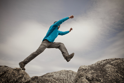 A hiker leaps between two granite rocks on the summit of Needle Peak, BC, Canada.